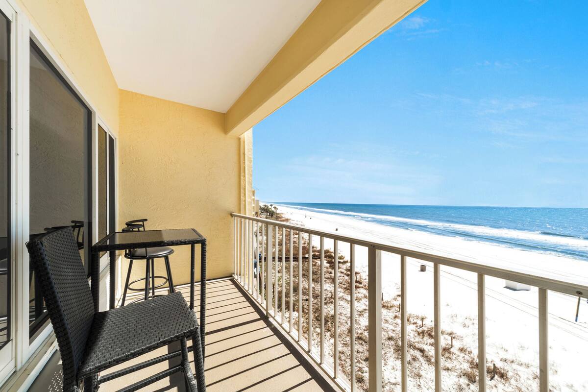 A balcony with a table and chairs, overlooking a beach with a railing.