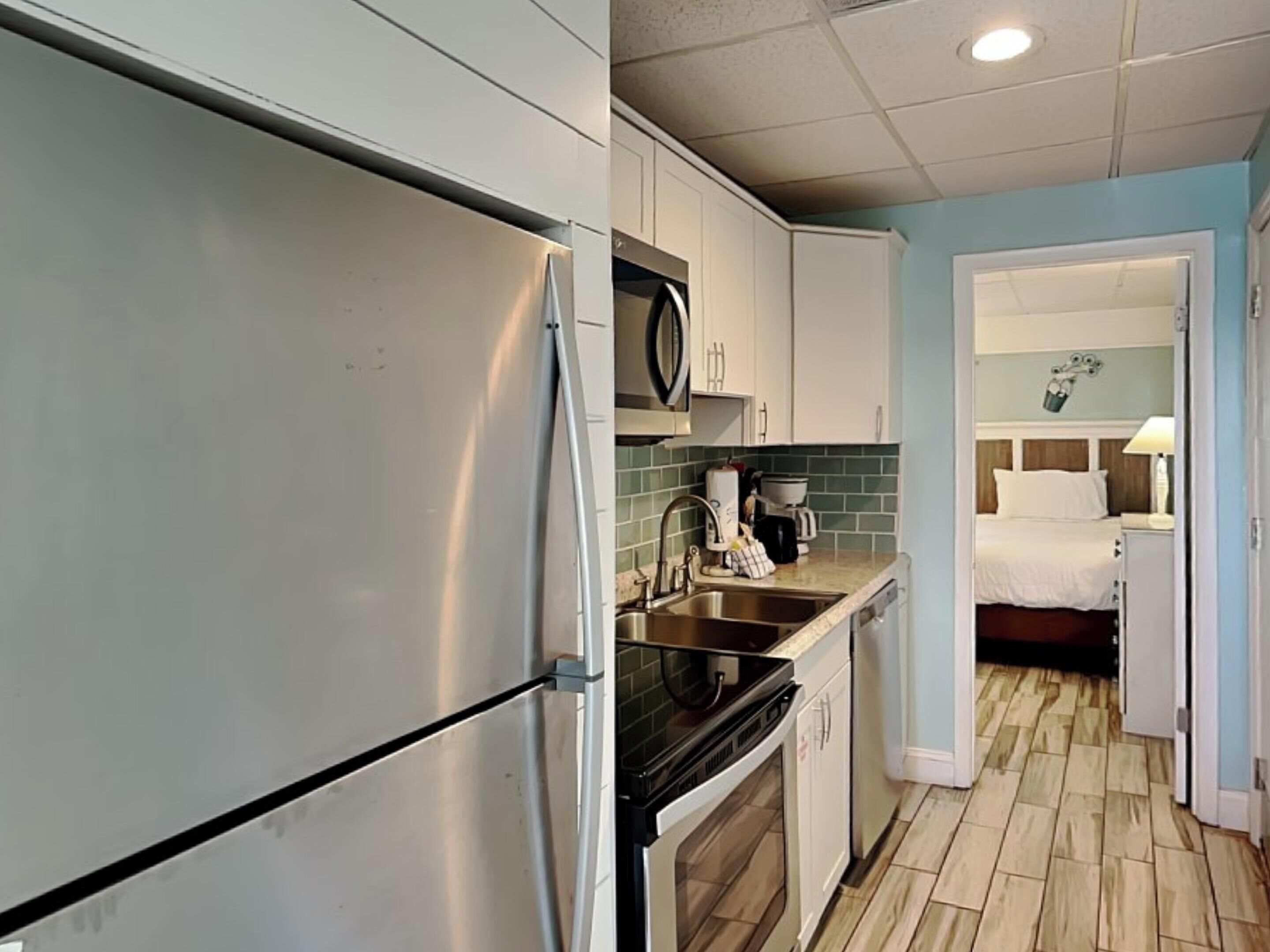 Cocina compacta con refrigerador, estufa y lavaplatos. Se ve una cama en la habitación contigua.