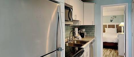 Cocina compacta con refrigerador, estufa y lavaplatos. Se ve una cama en la habitación contigua.