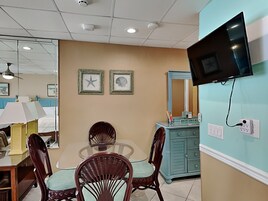 A hotel room with a dining area, a TV mounted on the wall, and two framed pictures on the wall.