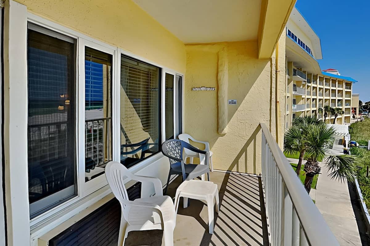 A balcony with white plastic chairs and a table, overlooking a building with multiple balconies and a clear blue sky.