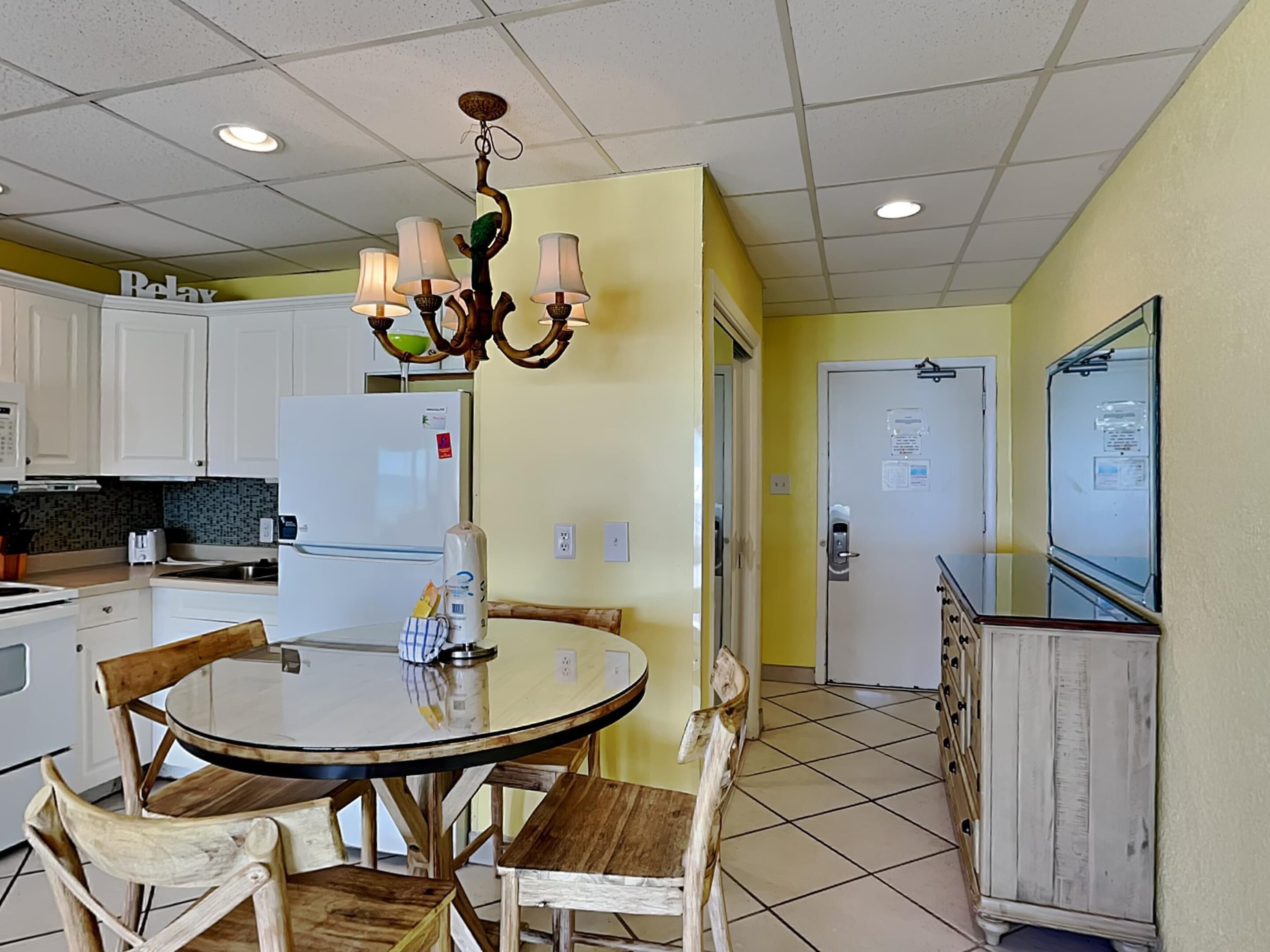 A kitchen with white cabinets, a round dining table with chairs, a chandelier, and a refrigerator.