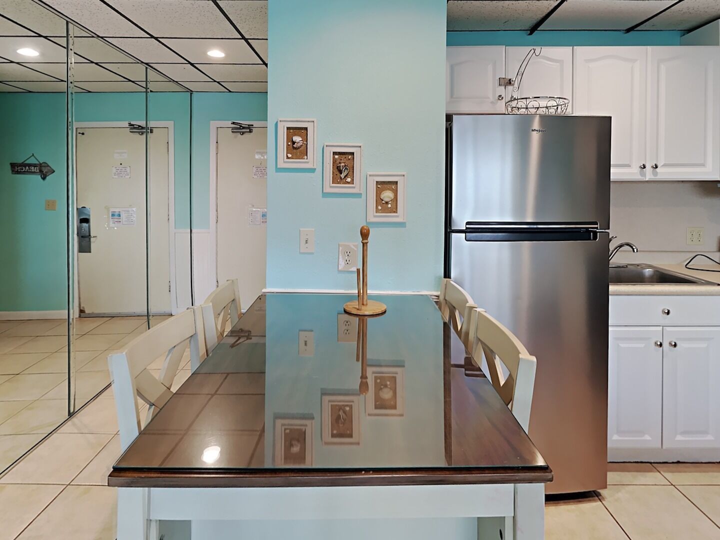 Eine moderne Küche mit Edelstahlkühlschrank, weißen Schränken und einem Esstisch mit Glasplatte und Stühlen.