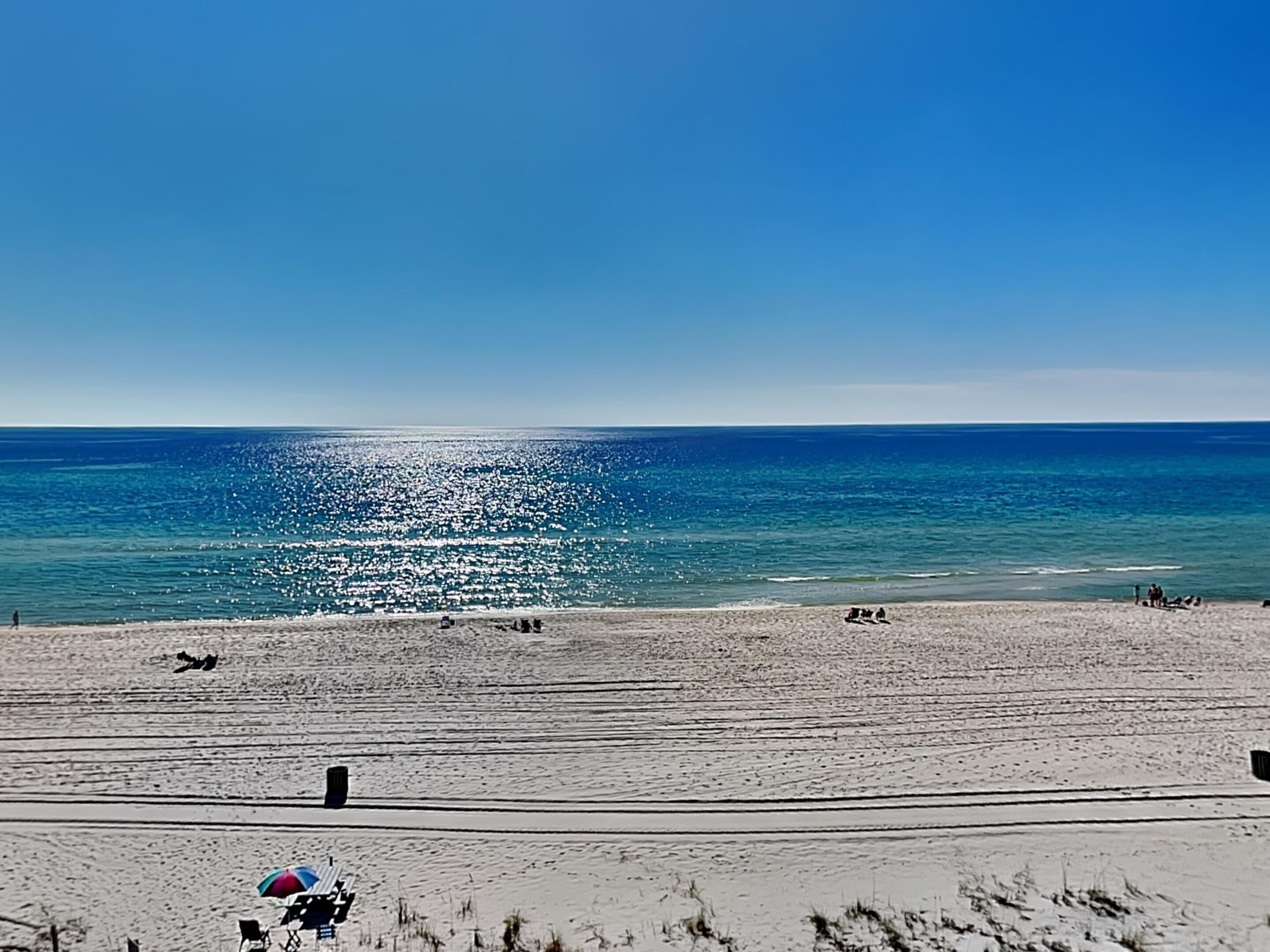 A beach with a clear sky, calm sea, and a few people and umbrellas.