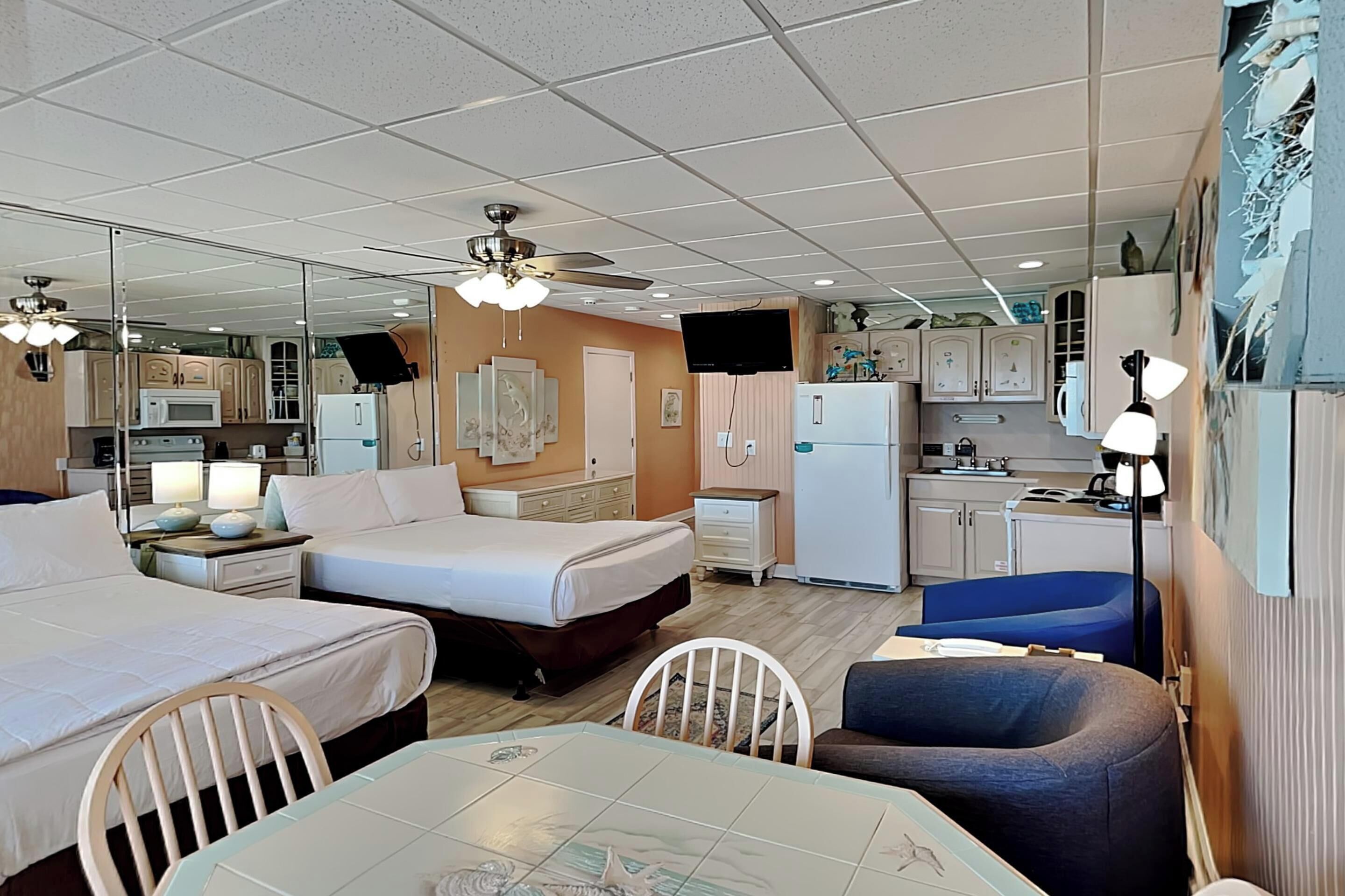 Een kleine hotelkamer met een bed, een kitchenette, een eettafel en een plafondventilator.