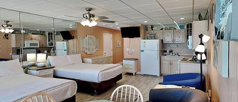 A compact hotel room with a bed, a small kitchenette, a dining table, and a ceiling fan.