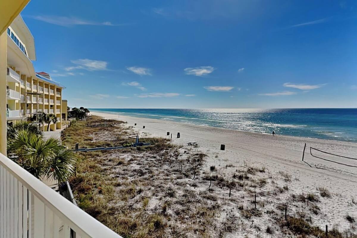 A beach view from a balcony with a building on the left, a sandy beach, and the ocean.