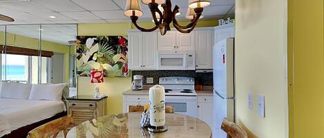 A hotel room with a bed, a round dining table with chairs, a kitchen area with a stove and microwave, and a ceiling with a chandelier.