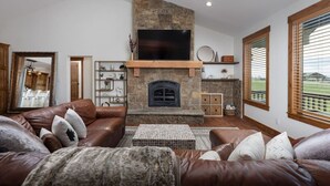 A living room with a stone fireplace, leather sofas, and a flat-screen TV. - Teton Time 4BR Home  - Hot Tub (Driggs)