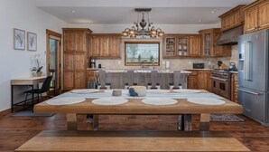 A modern kitchen with wooden cabinets, a central island with placemats, a built-in oven, and a stainless steel refrigerator. - Teton Time 4BR Home  - Hot Tub (Driggs)