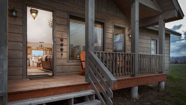 A wooden cabin with a porch, a visible kitchen area, and a door leading inside. - Teton Time 4BR Home  - Hot Tub (Driggs)