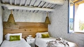 Une chambre avec deux lits, une tête de lit en bois, des paniers suspendus et une fenêtre donnant sur un beau paysage.