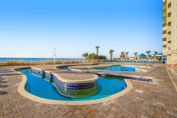 A swimming pool area with multiple pools, a beach view, and a building with balconies. - Wonderful 16th-floor oceanfront condo w/shared pool & hot tub, WiFi, AC (North Myrtle Beach)