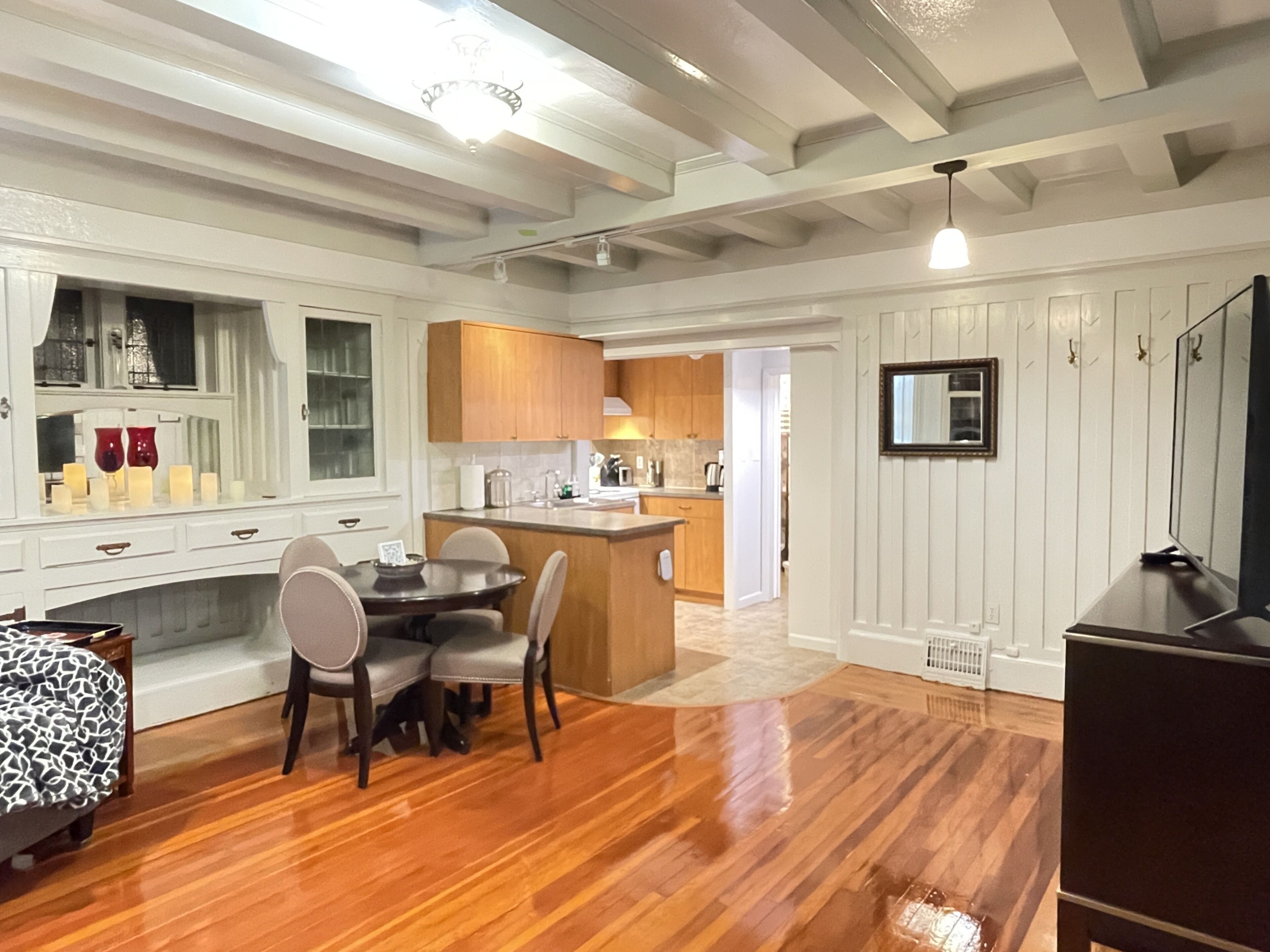 A modern kitchen with wooden cabinets, a dining area with a table and chairs, and a living room with a sofa and a TV.