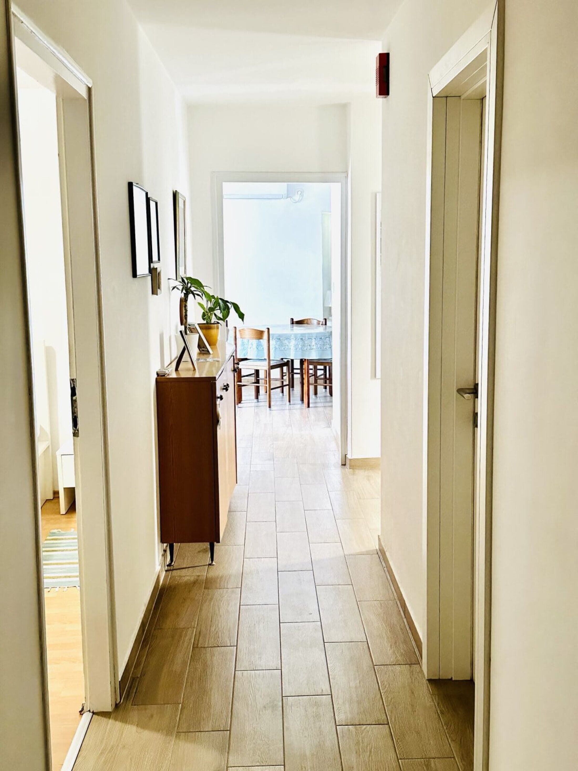 A hallway with a dining area at the end, featuring a table and chairs.