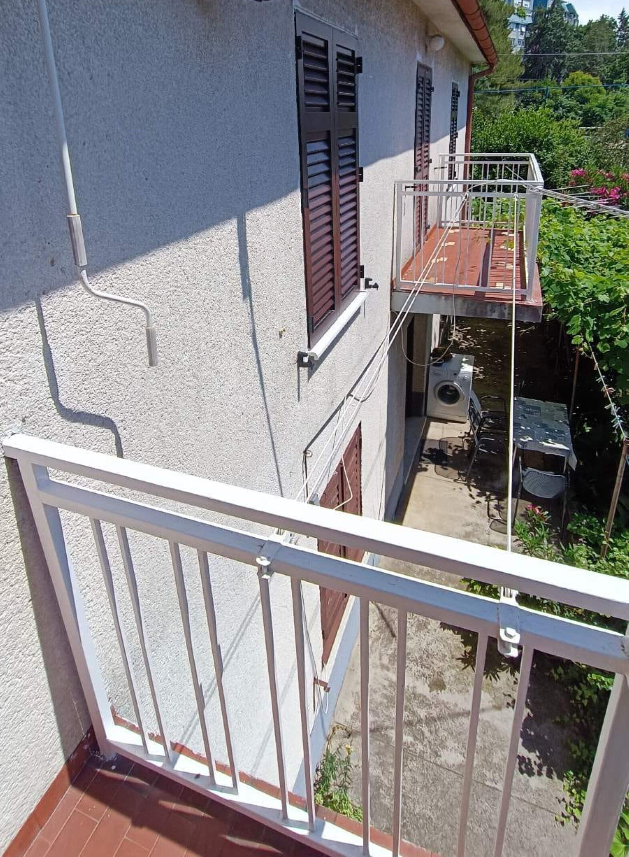 Een gebouw met twee verdiepingen, een balkon, een klein terras en een zichtbaar raam met luiken.
