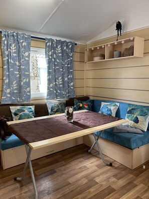 A cozy room with a wooden floor, a sofa with patterned cushions, a small table with a vase, and a shelf with decorative items.