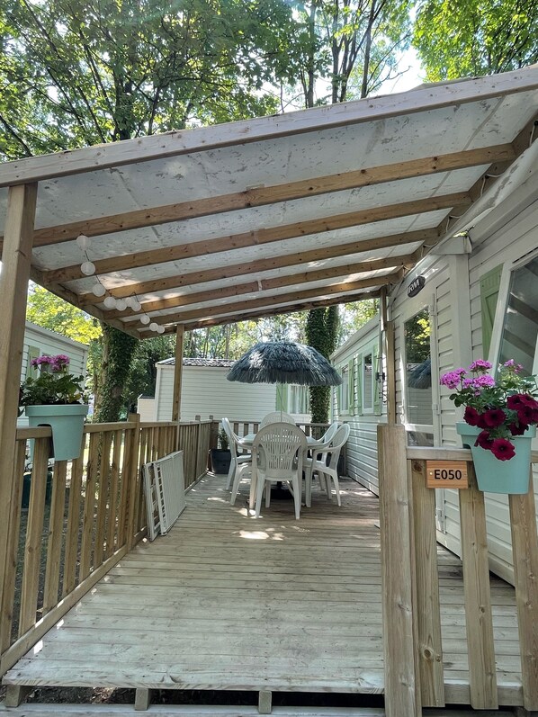 A wooden deck with a covered patio area, outdoor seating, and potted plants.