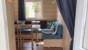 Ein kleines Zimmer mit einem Bett, einem Schreibtisch und einem Stuhl. Es gibt ein Fenster mit Vorhängen, eine Tür und eine Fußmatte.
