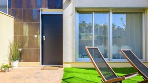 A modern building with a dark door, large windows, and two lounge chairs on a green lawn. - Residencial Oropesa - La Concha by Interhome (Oropesa del Mar)