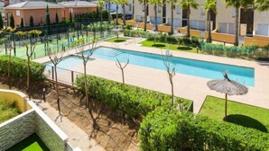 A pool area with a rectangular pool, surrounded by palm trees and greenery, with buildings in the background. - Residencial Oropesa - La Concha by Interhome (Oropesa del Mar)
