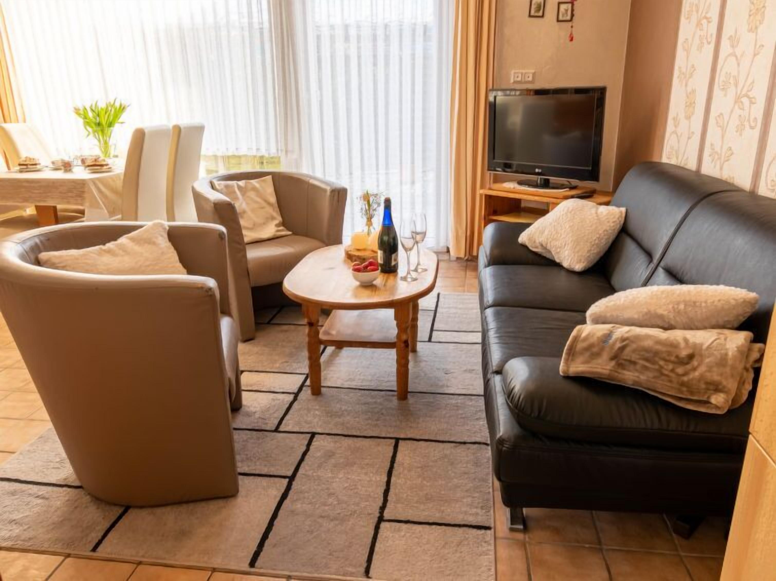 A living room with a sofa, two armchairs, a coffee table, a TV, and a dining area with a table and chairs.