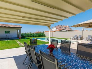 Une terrasse extérieure avec une piscine, un espace salon couvert et une table avec des chaises.