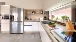 Une cuisine moderne avec un réfrigérateur en acier inoxydable, des armoires en bois et une fenêtre agrémentée de plantes.
