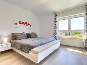 Une chambre à coucher moderne avec un lit, une table de chevet, une fenêtre donnant sur un beau paysage et un tableau accroché au mur.
