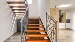 Un escalier moderne avec des marches en bois et des rampes en métal, menant à un espace cuisine doté de meubles en bois et d’un four encastré.