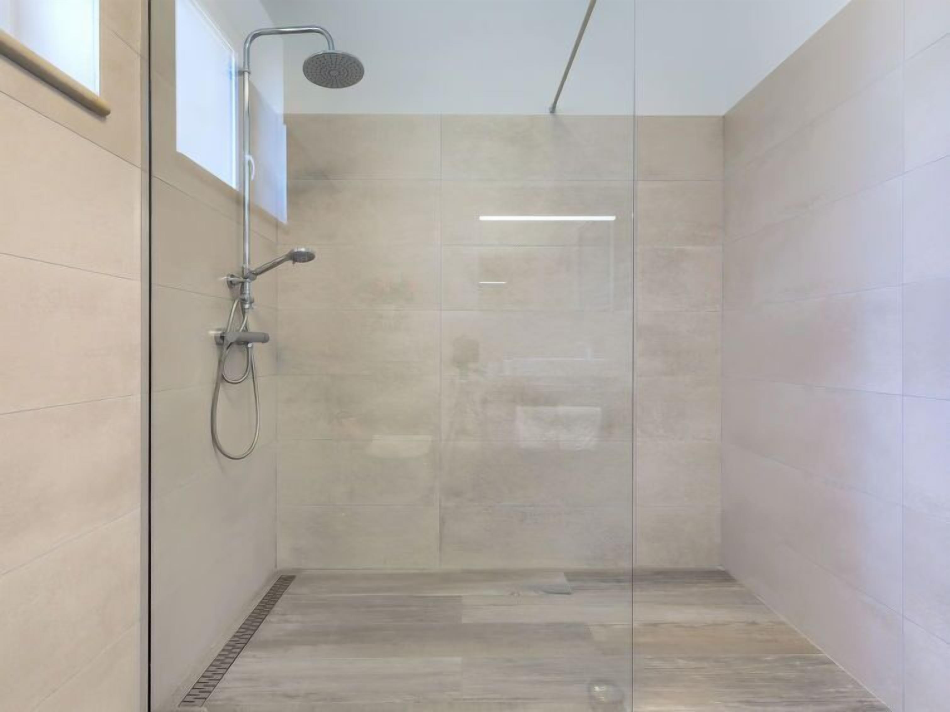 A modern shower with a glass door, a handheld showerhead, and a wall-mounted faucet.