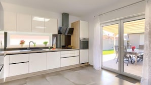 Une cuisine moderne avec des armoires blanches, une hotte de cuisinière en acier inoxydable et une grande fenêtre donnant sur un espace patio.
