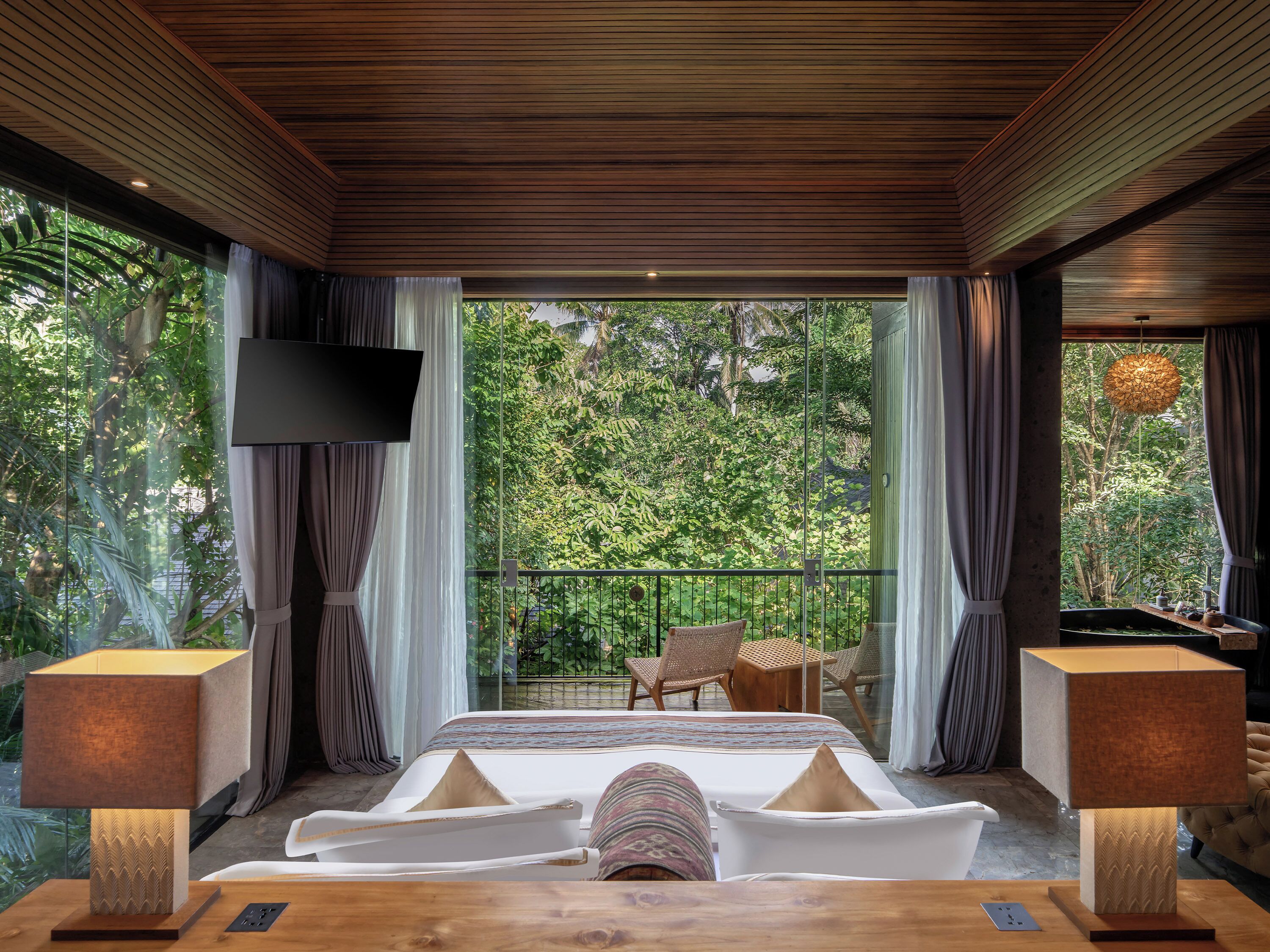 A bedroom with a large bed, a TV, and a balcony with chairs and a table.