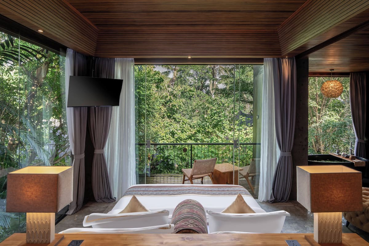 A bedroom with a large bed, a TV, and a balcony with chairs and a table.