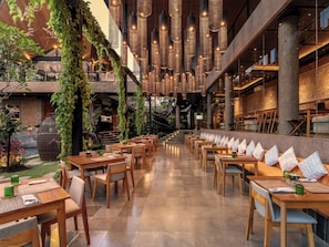Ein Restaurant mit Holztischen und -stühlen, hängenden Lampen und Grünpflanzen.