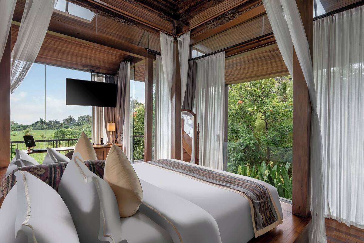 A bedroom with a large bed, a TV, and a view of a green landscape.
