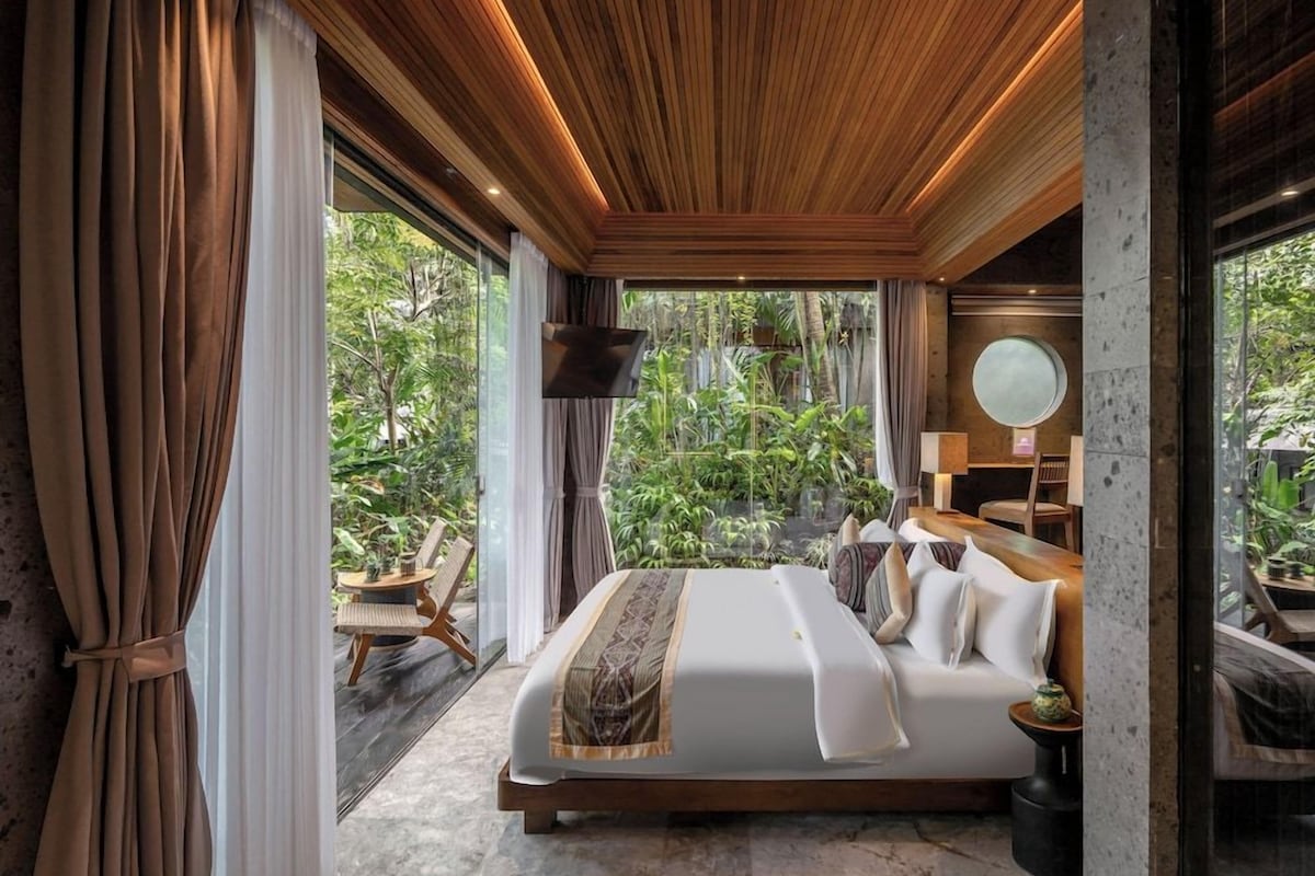 Une chambre moderne avec un grand lit, un plafond en bois et une vue sur la verdure environnante.