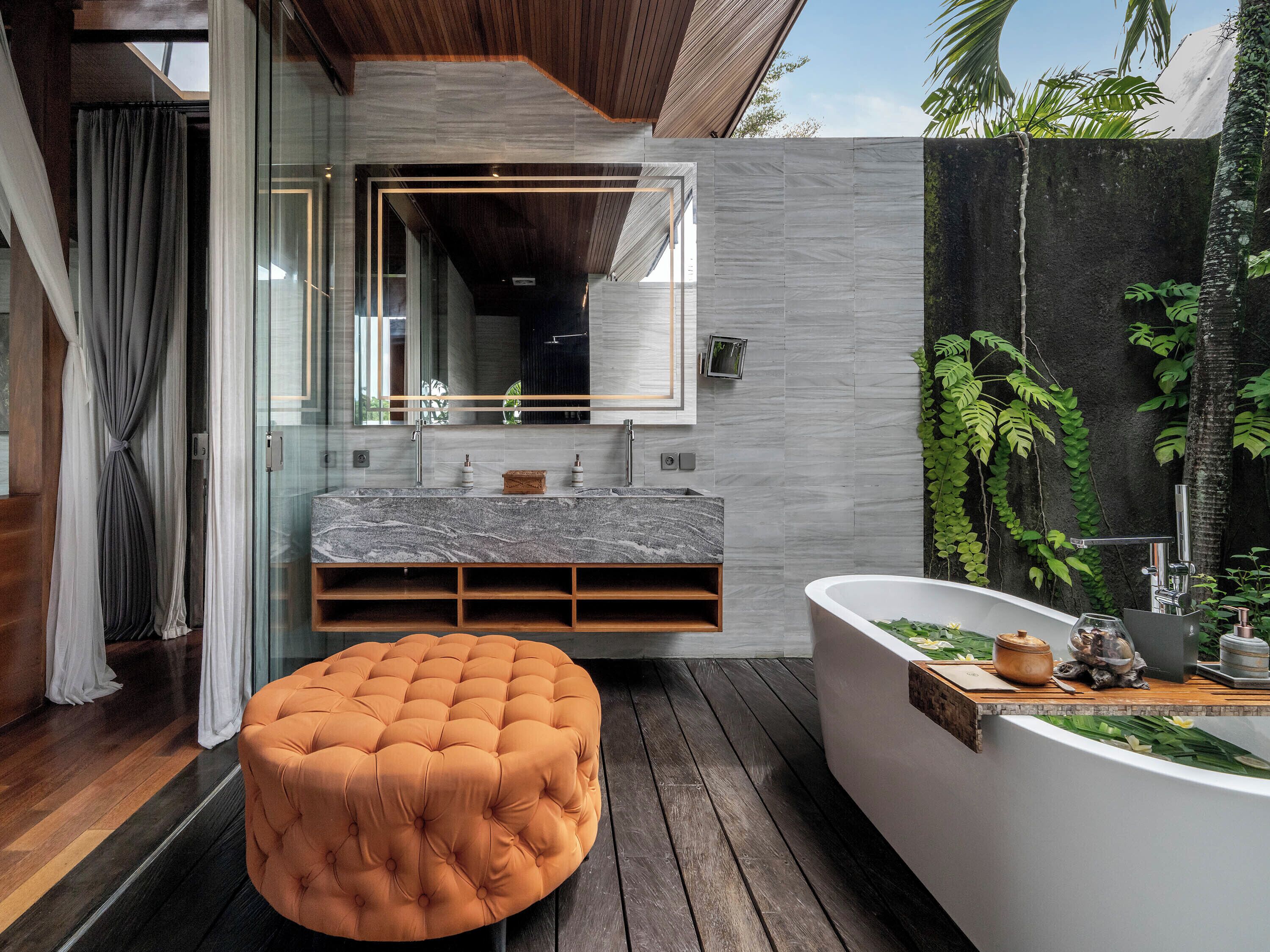 A modern bathroom with a marble vanity, a round ottoman, and a freestanding bathtub.