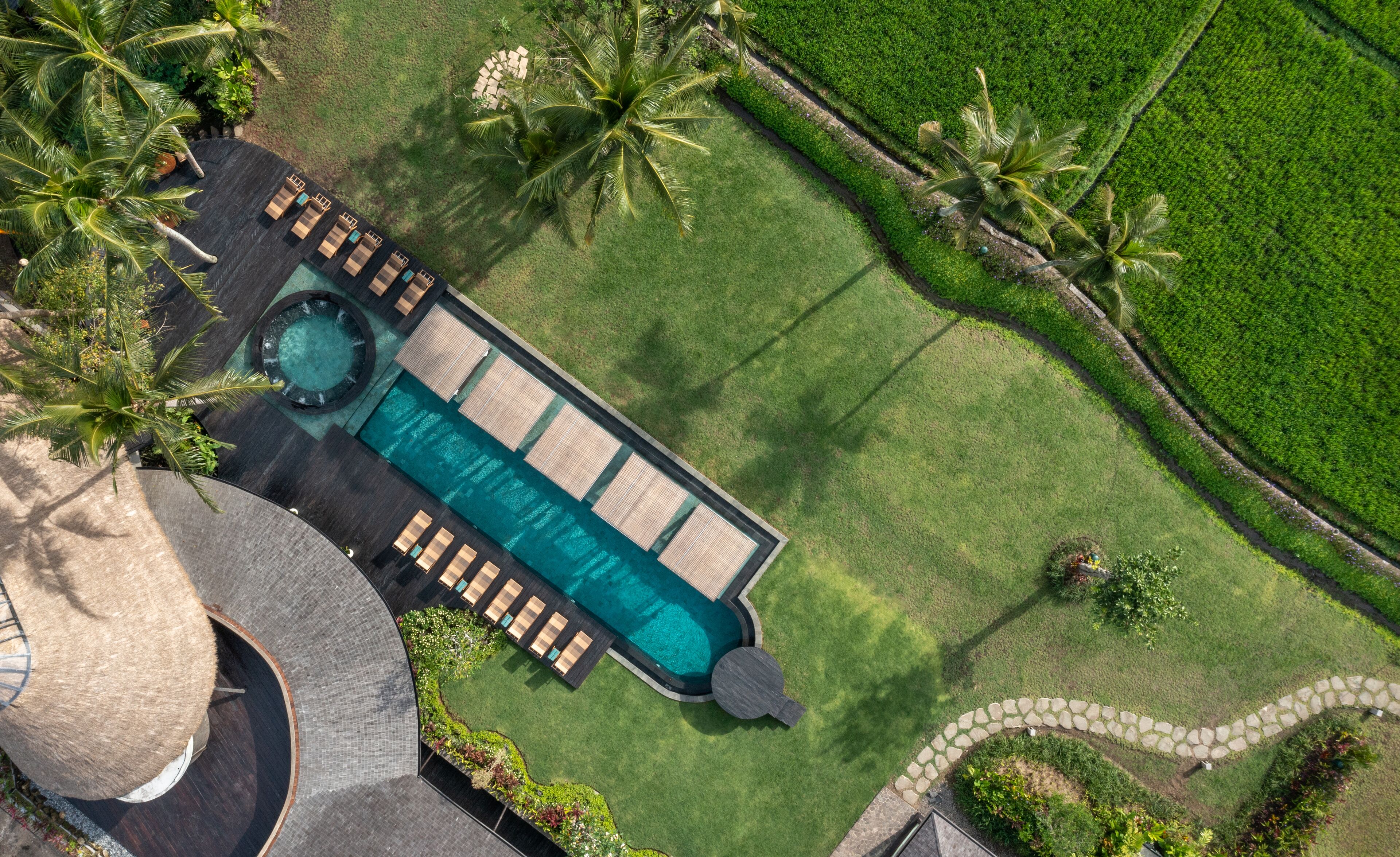 An aerial view of a resort with a swimming pool, lounge area, and palm trees.