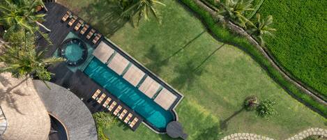 An aerial view of a resort with a swimming pool, lounge area, and palm trees.