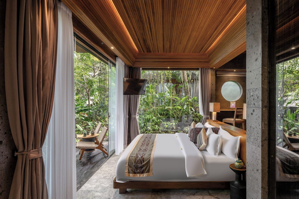 A bedroom with a bed, a TV, a round mirror, and a view of greenery.