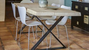 Un coin repas avec une table en bois rustique, des chaises blanches et un luminaire suspendu en fibres tressées.