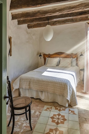 Una camera da letto con una testiera in legno, un letto con copripiumino trapuntato, una sedia in vimini e un pavimento a motivi.