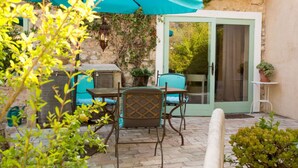 Une terrasse avec une table et des chaises, un parasol de couleur turquoise et une porte donnant sur un jardin.