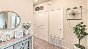 A hallway with a mirror, a clock, framed photos, a potted plant, and a wall-mounted artwork. - Brand-New Townhome Near UNT/TWU & The Square! (Denton)