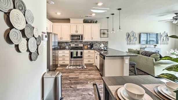 A modern kitchen with white cabinets, a central island, and a dining area with a table and chairs. - Brand-New Townhome Near UNT/TWU & The Square! (Denton)