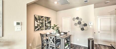 A dining area with a table set for four, surrounded by chairs, a rug, and a wall-mounted shelf with decorative items.