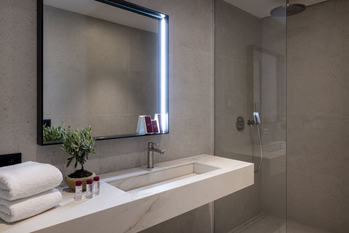 A modern bathroom with a large mirror, a white sink, a potted plant, and a glass-enclosed shower.