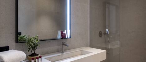 A modern bathroom with a large mirror, a white sink, a potted plant, and a glass-enclosed shower.