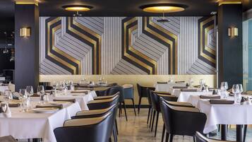 A restaurant with tables set for dining, featuring a geometric wall design and modern lighting.